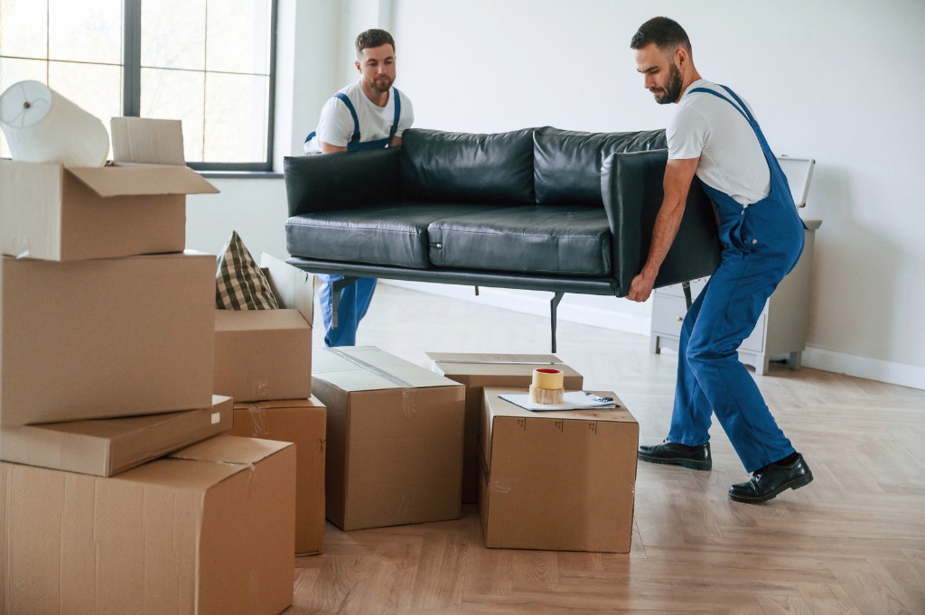 Professional movers carrying a sofa through an apartment with moving boxes